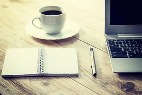 laptop, cup of coffee, open notebook and pen on the table