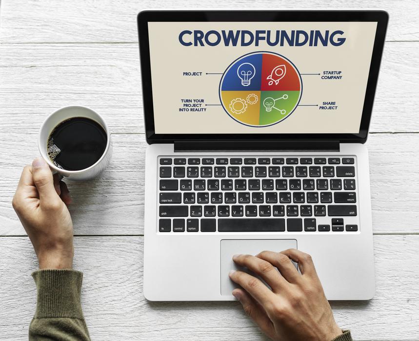 Person with the cup of coffee, looking for crowdfunding on the laptop