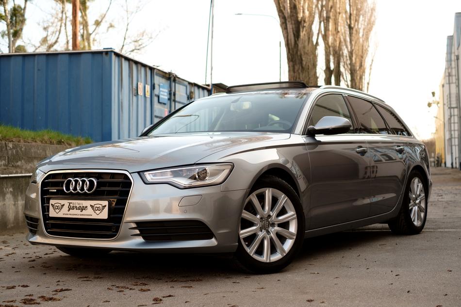 Beautiful, shiny, grey Audi car on the road, near the trees and blue fence