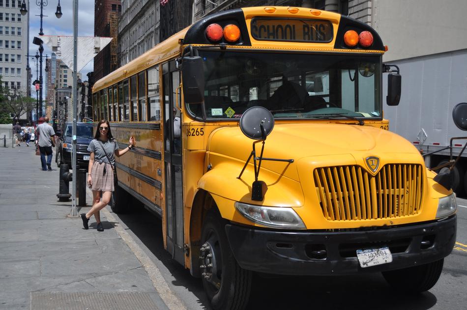 Woman, near the yellow and black bus, on the road, among the buildings