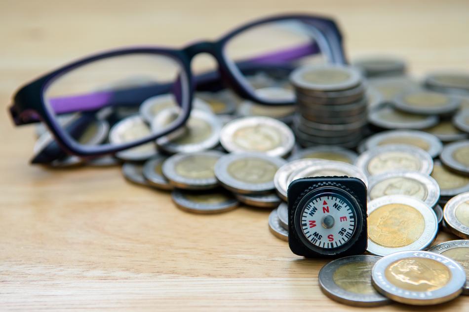 coins with compass next to glasses on blurred background