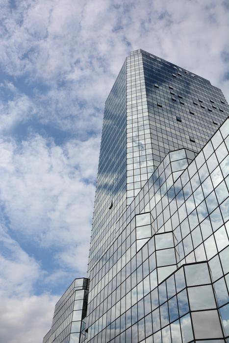 Shiny, glass building with the reflections of the blue sky with white clouds