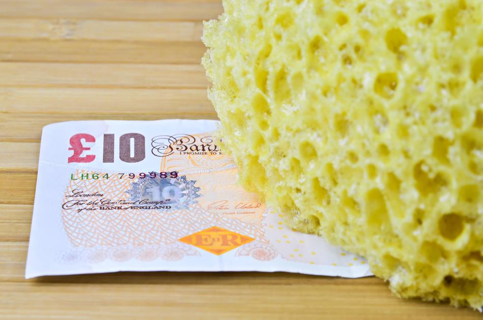 Yellow sponge in light, near the colorful banknote, on the wooden surface