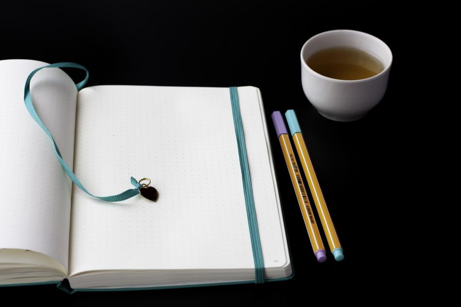 a cup of tea with pens near a notebook