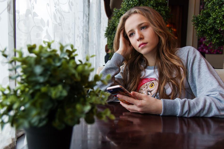 photo of a pensive girl with a smartphone by the window