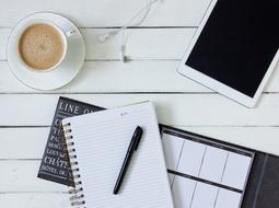 notebook, schedule, pen, tablet and cup of coffee on a white table