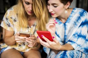 two young women sit Together looking at Phones