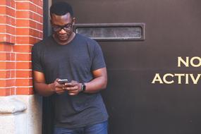 african american with phone near brick wall