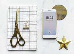 scissors on a notebook and an iPhone on a table