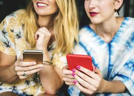 two girlfriends are holding smartphones in their hands