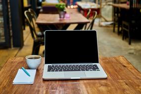 Laptop, white cup of coffee and notebook with a pen on the beautiful wooden table