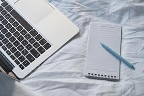 laptop, notebook and pen on the bed