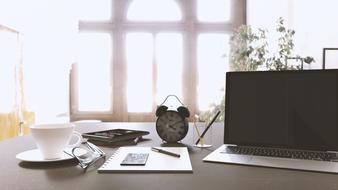 alarm clock, laptop, coffee cup and glasses on the desktop