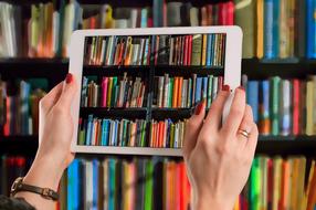 tablet in female hands at bookshelves