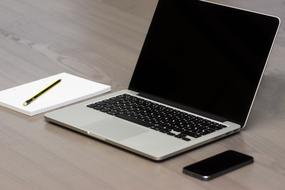 Laptop, smartphone and notebook with a pen on the wooden surface