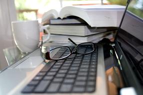 Books, white cup and glasses on a laptop