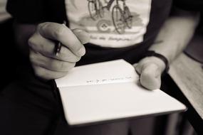 Black and white photo of a person with watch writing notes in the notebook