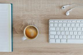 Mac keyboard and black coffee near the headphones and notebook on the wooden table