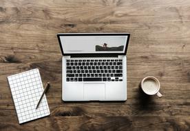 Checkered paper with the pen, near the laptop and cup of coffee, on the wooden table