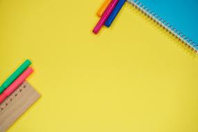 Colorful felt-tip pens, ruler and blue notebook, on the yellow table