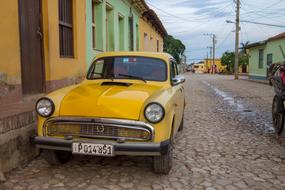 Yellow Old Car parked in the street at one-storey building, Cuba