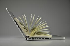 Book, laying on the shiny laptop, at grey background