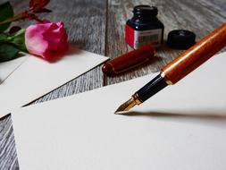 fountain pen, white sheet of paper and pink rose