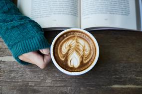 cup of cappuccino, hand, sweater and open book