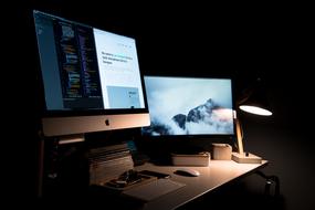 Colorful Apple Mac monitors with the keyboard and mouse, and books on the desk, with the light