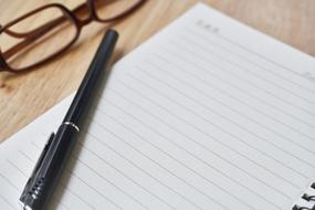 black pen on a notebook and glasses on a table