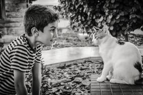 Black and white photo of the boy communicating with a cat among the plants
