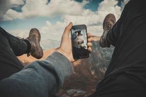 person with smartphone in hand above mountains