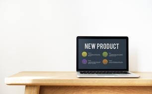 Laptop with the "New Product" sign and colorful icons, on the wooden table, in light