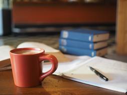 Coffee in red mug in front of notebook and books, Homework