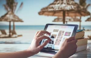 Person, using laptop, on the beautiful, sandy beach with the umbrellas, near the ocean