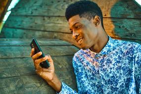 photo of african guy with a smartphone on a background of a wooden coil