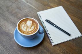 Coffee in blue cup and notepad on desk