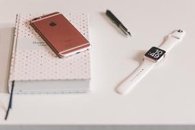 iPhone on a diary, a smart watch and a pen on the table