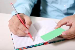 man is writing on a notebook