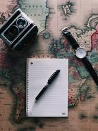 retro camera, watch and notebook with pen on the map