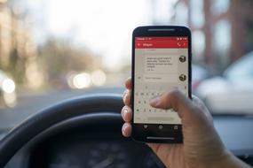 smartphone with text message in male hand at steering wheel