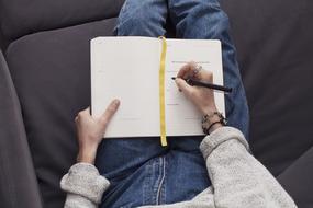 girl makes notes in a notebook while lying on a sofa