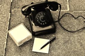 Old black desk Phone near pen on stack of blank paper