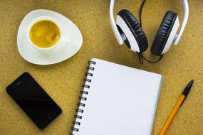 iPhone, espresso, headphones and a notebook with a pen on the table