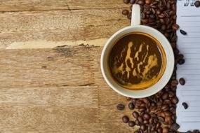 Beautiful, white cup of coffee and beans, on the wooden surface
