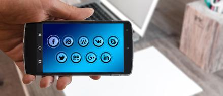 Blue icons on the screen, of the black smartphone, in the hand, near the laptop