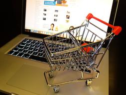 Metal shopping cart with red handle, on the grey and black laptop with keyboard lighting