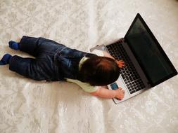 kid playing with laptop on bed