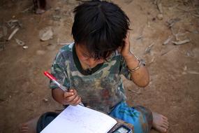 poor child draws on a notebook outdoors