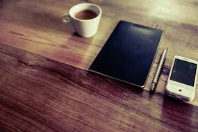 Beautiful tablet, smartphone, pen and white cup of coffee on the wooden surface